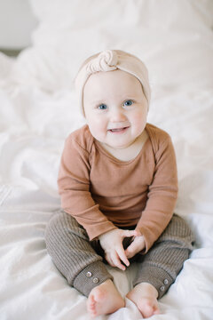 Baby girl sitting up on bed and smiling at camera