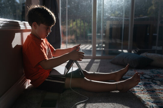 Boy using ipad tablet on the floor of his home with sun in window