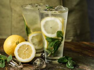 Lemonade drink with ice, mint and lemon on table background with cooking ingredients - 356489800