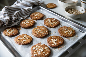 Freshly baked homemade oatmeal cookies on baking tray on white kitchen table.