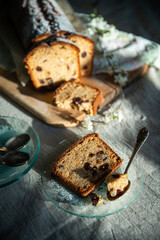 Sliced homemade pound cake with dried berries, vintage glass plates and blooming cherry twigs on linen tablecloth.