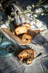 Sliced homemade pound cake with dried berries, vintage glass plates and blooming cherry twigs on linen tablecloth.