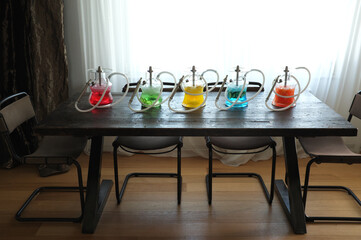 Several colorful arranged hookahs on a wooden table with a window in the background.