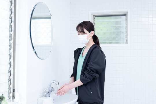 黒いジャージを着てマスクをして手を洗っている日本人女性