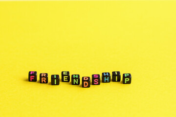 The word friendship composed from cubes with multicolored letters on a yellow background. A close-up.