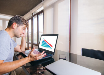 Young man worried in front of laptop with bad economic results on the screen