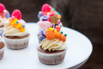 Chocolate cupcakes with cream cheese frosting, chewing marmalade, sweets and golden topper on dark background