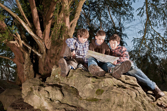three boys reading map on top of rock