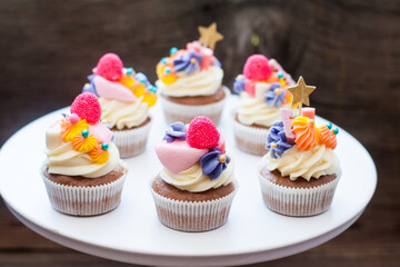Chocolate cupcakes with cream cheese frosting, chewing marmalade, sweets and golden topper on dark background