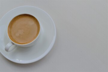 Composition of a white round cup with coffee standing on a saucer (left) and a light gray background for inscription