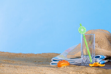 On the sea beach lies a hat and an empty glass with a straw for a cool drink. Blue beach towel.