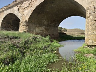 Fototapeta na wymiar Old soviet stone cracked bridge. Muddy river. Green grass. Blue sky. Olishkany - Moldova