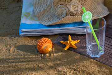 On the sea beach lies a hat and an empty glass with a straw for a cool drink. Blue beach towel.