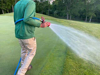 Water is sprayed on a golf green by a maintenance worker