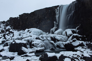 Amazing waterfall flowing down from volcanic black rocks covered by snow