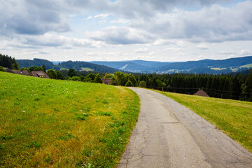 Fototapeta na wymiar picturesque panorama with deserted road between sloping meadows in the High Black Forest landscape in Breitnau, Baden-Württemberg, Germany on a cloudy day in summer