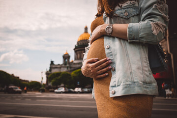 Pregnant woman in dress holds hands on belly on a white background. Pregnancy, maternity, preparation and expectation concept. Close-up, copy space. Beautiful tender mood photo of pregnancy.