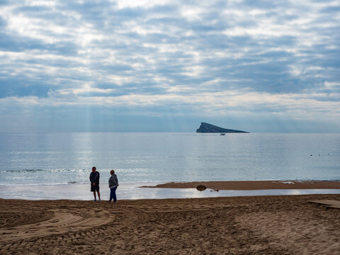Pareja contemplando el atardecer desde la orilla de la playa con la isla de Benidorm al fondo