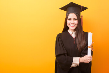 Portrait of happy Beautiful woman in graduation gown is holding education certificate on yellow...
