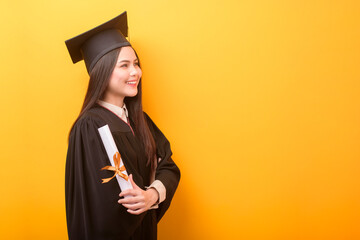 Portrait of happy Beautiful woman in graduation gown is holding education certificate on yellow...