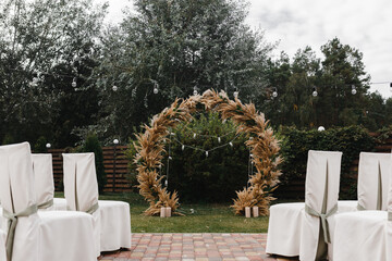 Wedding arch decorated with flowers and lights and chairs for guests. Wedding ceremony. Wedding arch