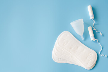 Sanitary pad, menstrual cup and tampons on blue background. Concept of feminine hygiene during...