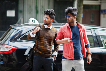 Two young stylish indian man frieds model posing in street against black taxi car.