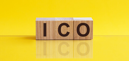 ICO abbreviation stands for Initial Coin Offering on wooden blocks, yellow background....