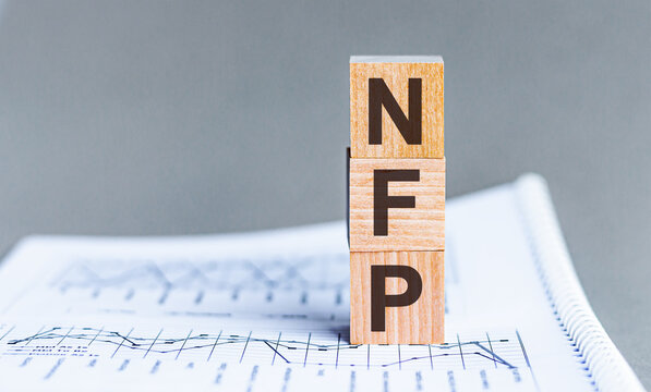 Word NFP - Non Farm Payrolls - acronym concept on cubes and diagrams on a gray background. Business as usual concept image.