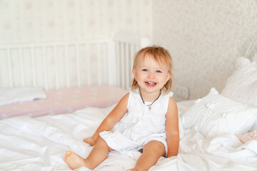 Naklejka premium little girl on bed in bedroom and laughs. happy childhood.