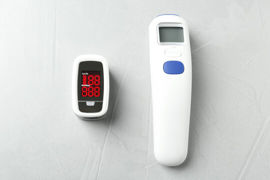 Modern Fingertip Pulse Oximeter And Non Contact Infrared Thermometer On Light Grey Stone Background, Flat Lay