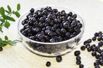 forest Northern blueberry lies in a transparent plate on a light wicker background, other berries are scattered on the table