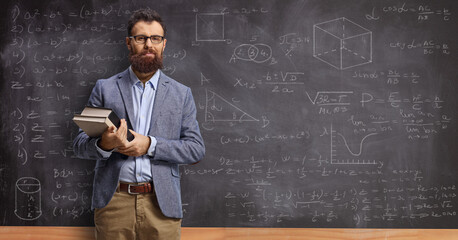 Male teacher holding books in front of a blackboard