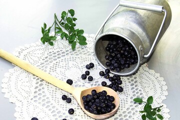 Fototapeta na wymiar Fresh blueberries are poured out of a metal canister into a wooden spoon lying on a light lace napkin