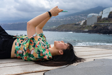 Young Asian tourist woman is chatting lying on her back. She is located on the Martianez beach, in Puerto De La Cruz, Tenerife.
