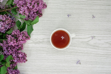 Fototapeta na wymiar Lilac and a cup of tea on a gray wooden background. There's a lilac flower in the cup.