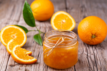 Orange jam in glass jar on wooden background.