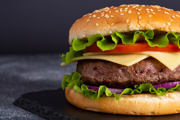 Tasty homemade burger with beef, tomatoes, onions, cheese and salad on a black stone background with copy space. Side view. fast food. Closeup. focus on cutlet