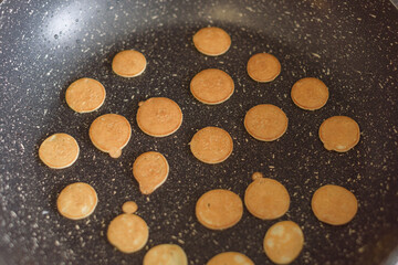 Tiny pancake cereal are fried in a ceramic pan