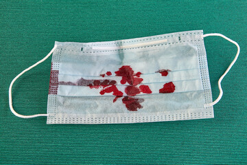 Bloodied surgical mask on a green background.