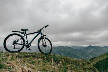 Obraz premium Горный велосипед на вершине горы, в дали видны горы и облака . 