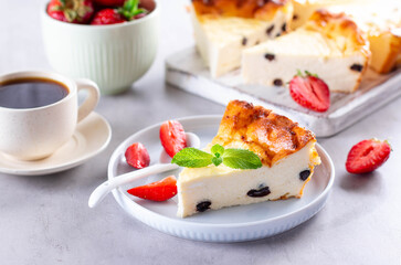 Cottage cheese casserole with raisins, mint and strawberries on gray cement background
