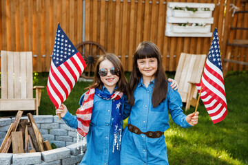 Two beautiful school-age girls spend time in the yard, holding USA flags