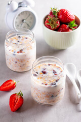 Granola breakfast in glass jars with yogurt or milk on gray cement background with alarm clock