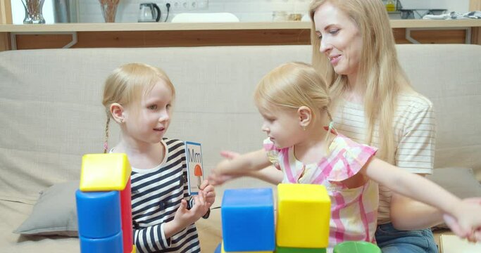 Cute girl showing cards with letters and pictures to little sister and mom. Learning the alphabet during the game. Preschool education.