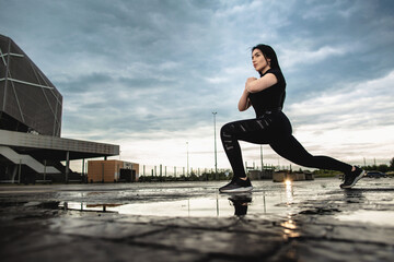 Bottom view, young sporty brunette is training outdoors. Woman makes lunges outdoors. Fitness, workout, sport concept