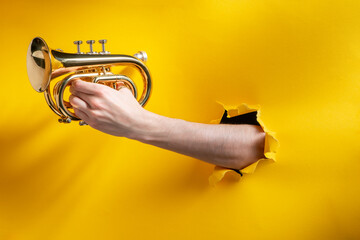 Hand playing horn through a torn hole in yellow paper background
