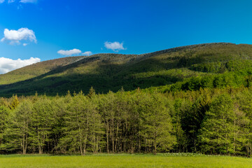 Mountainous landscape and Radhost hill during a sunny day with clouds in the sky.