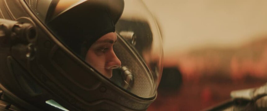Caucasian female astronaunt checking hud on her suit while exploring planet surface, Mars rover in the background