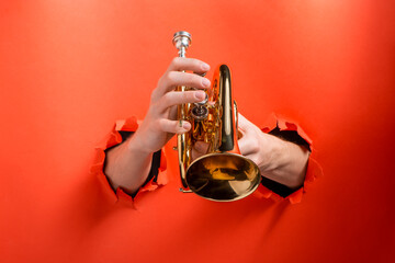 Hands playing pocket trumpet torn holes in red paper background